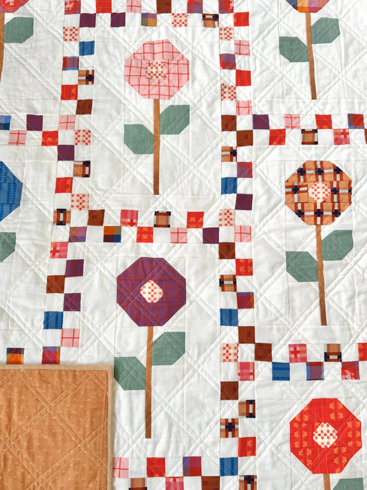 Photo of a floral quilt with vertical rectangles and a scrappy, checkerboard sashing